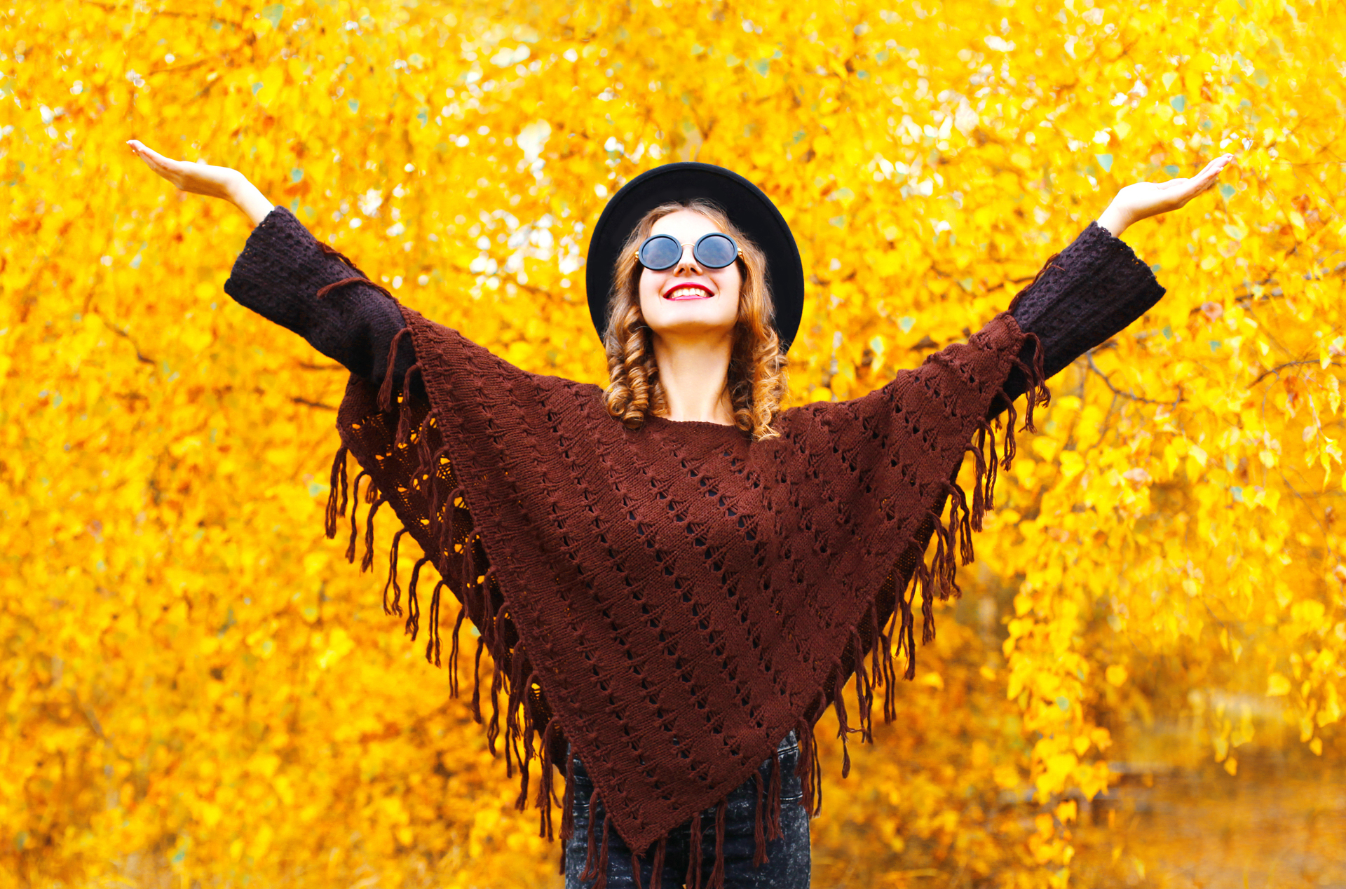 Fashion smiling woman enjoys an autumn park in black round hat, knitted poncho